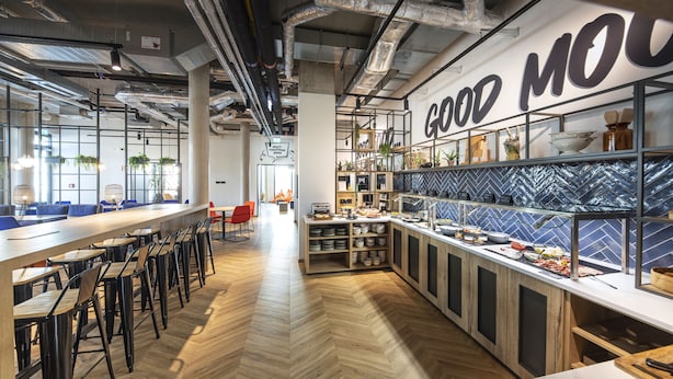 A modern cafe with a herringbone wood floor, bar seating, and a counter displaying food items. - Loginn Hotel Waiblingen (Waiblingen)