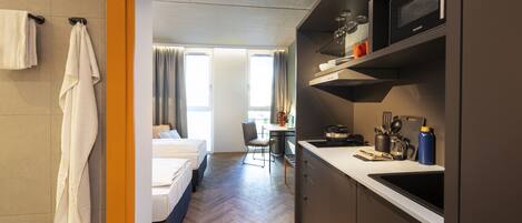 Una habitación de hotel moderna con kitchenette, una cama, un escritorio y vistas a la ciudad.