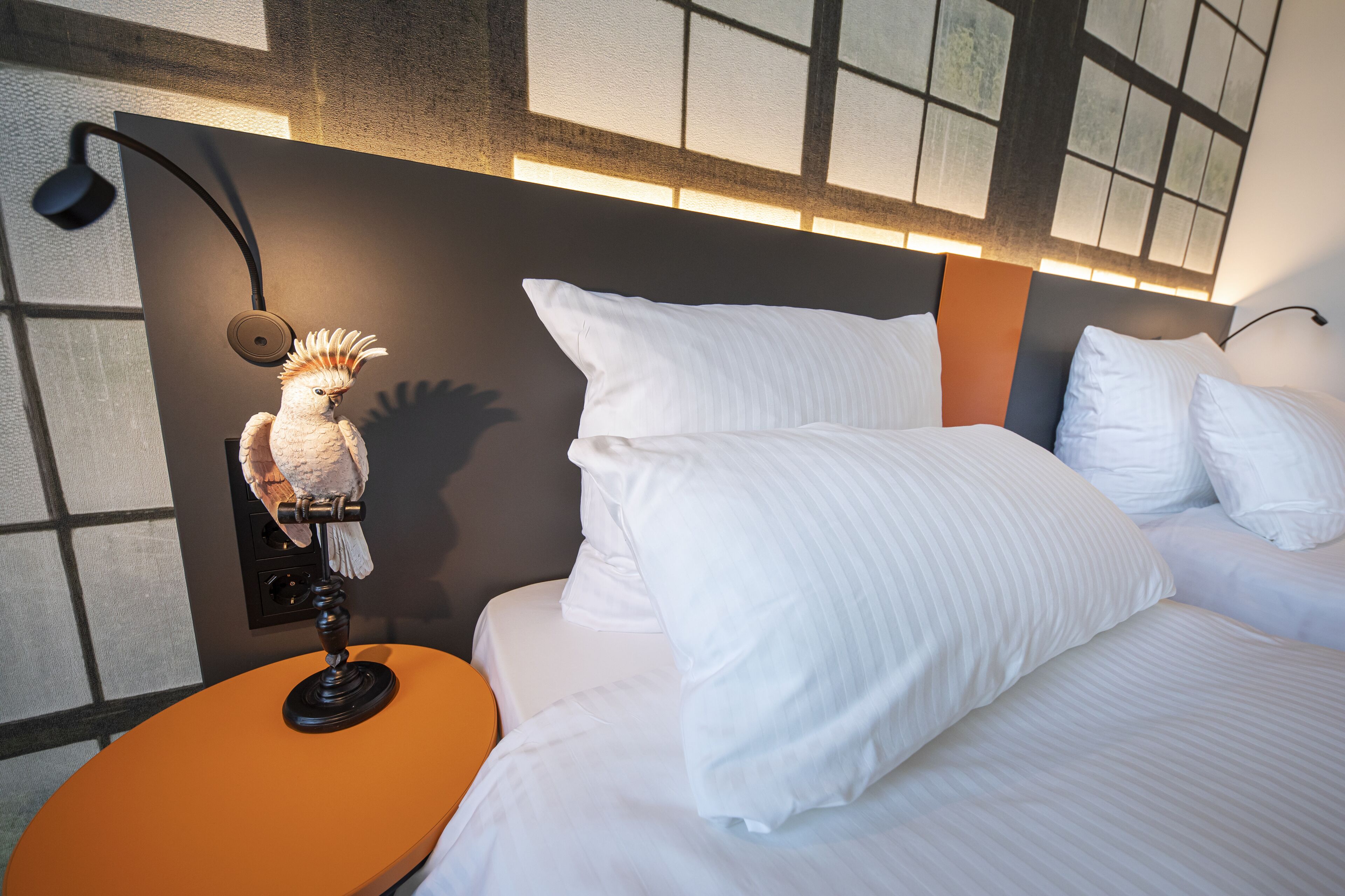 A hotel room with a bed, white pillows, a nightstand, a lamp, and a decorative bird statue.