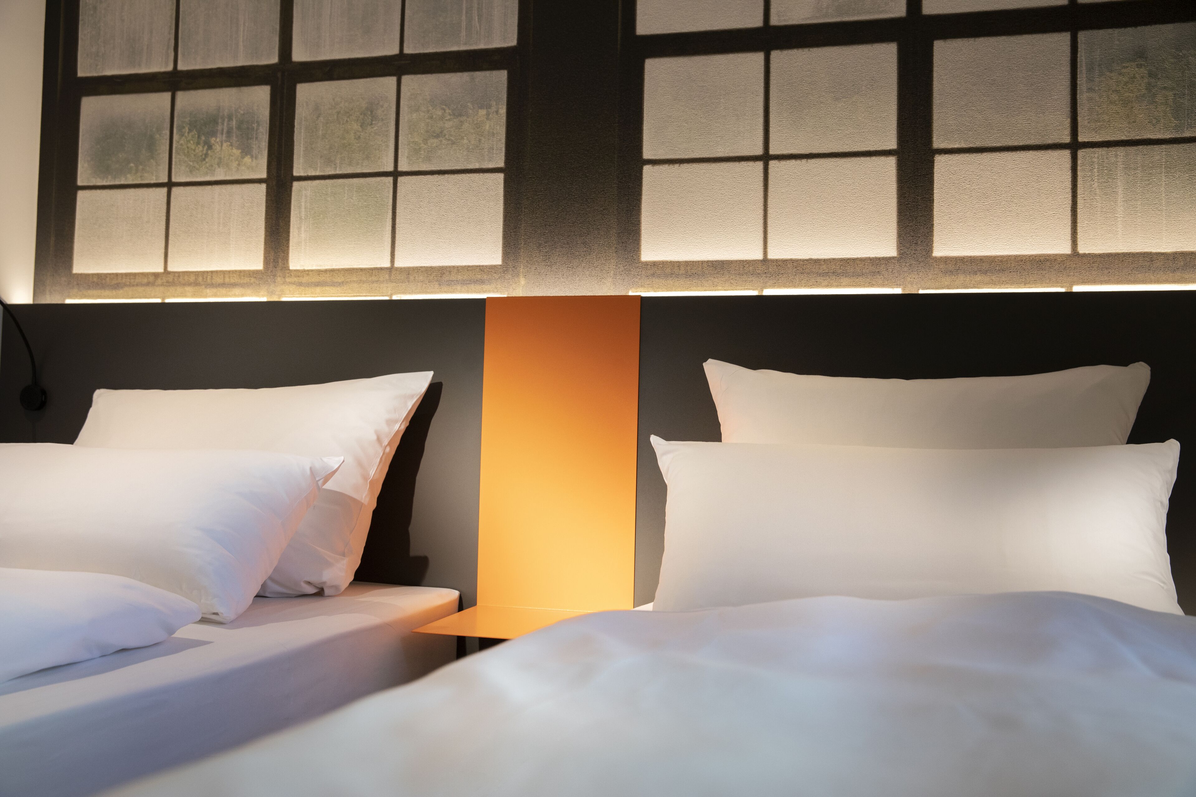 A hotel room with two beds, a nightstand, and a large window with a view.