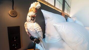 Un oiseau était perché sur un support dans une pièce où se trouvaient un lit et un luminaire fixé au mur.