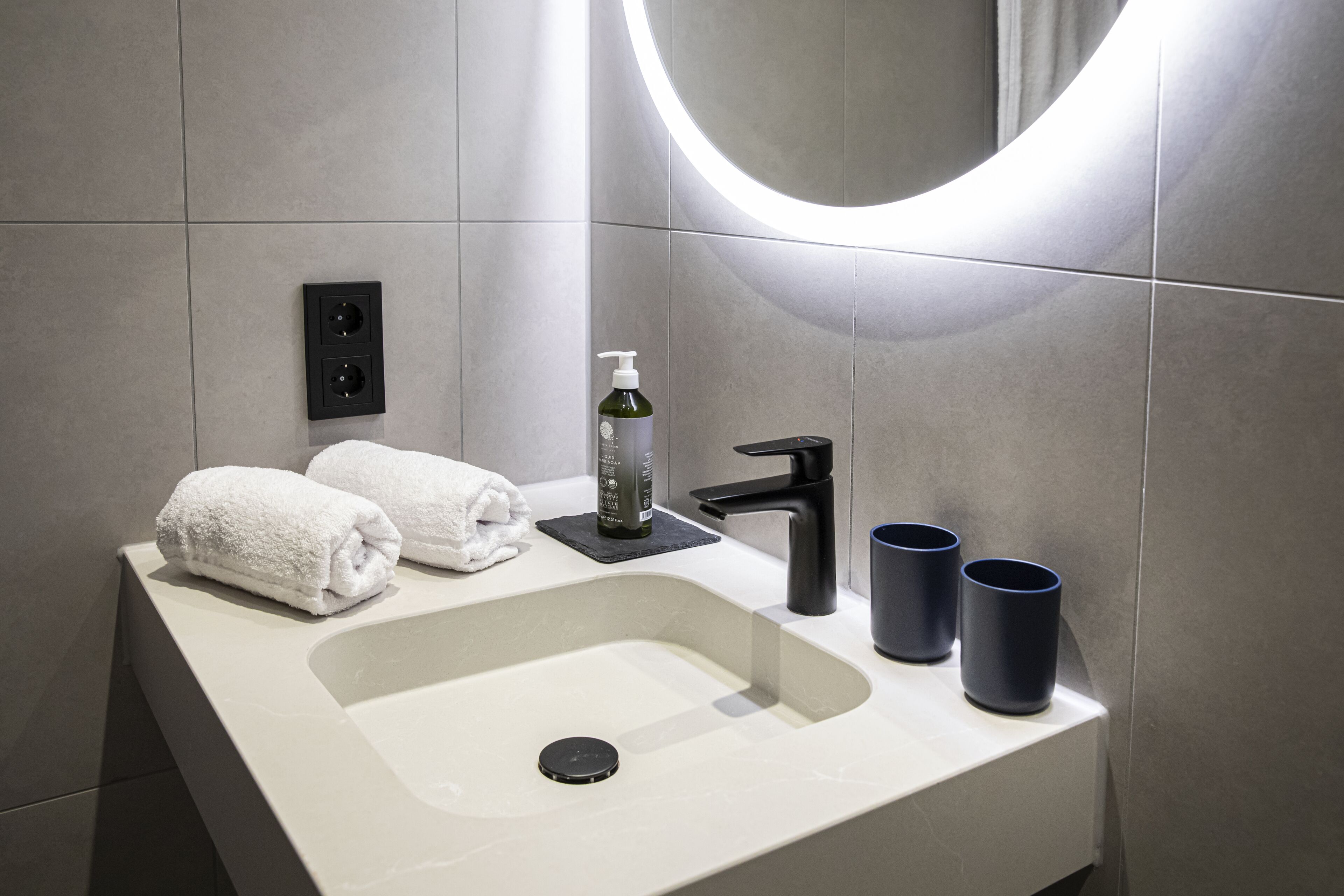 Une salle de bain moderne avec un lavabo blanc, un robinet noir et deux tasses bleu foncé.