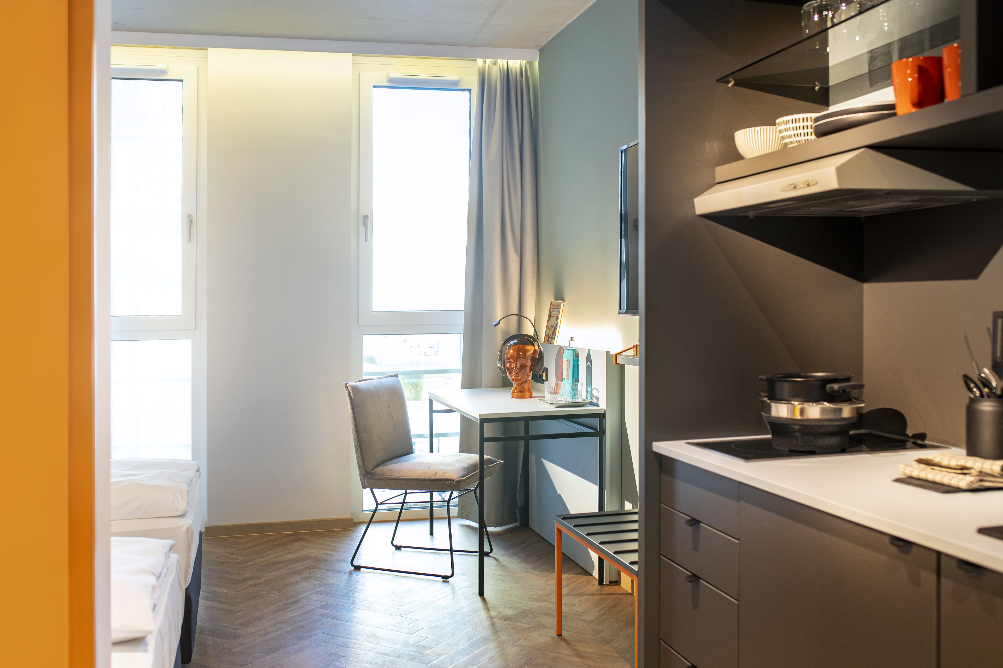 Une cuisine compacte avec un coin repas, une petite table et une chaise. On y trouve une fenêtre avec des rideaux, un évier et une cuisinière.