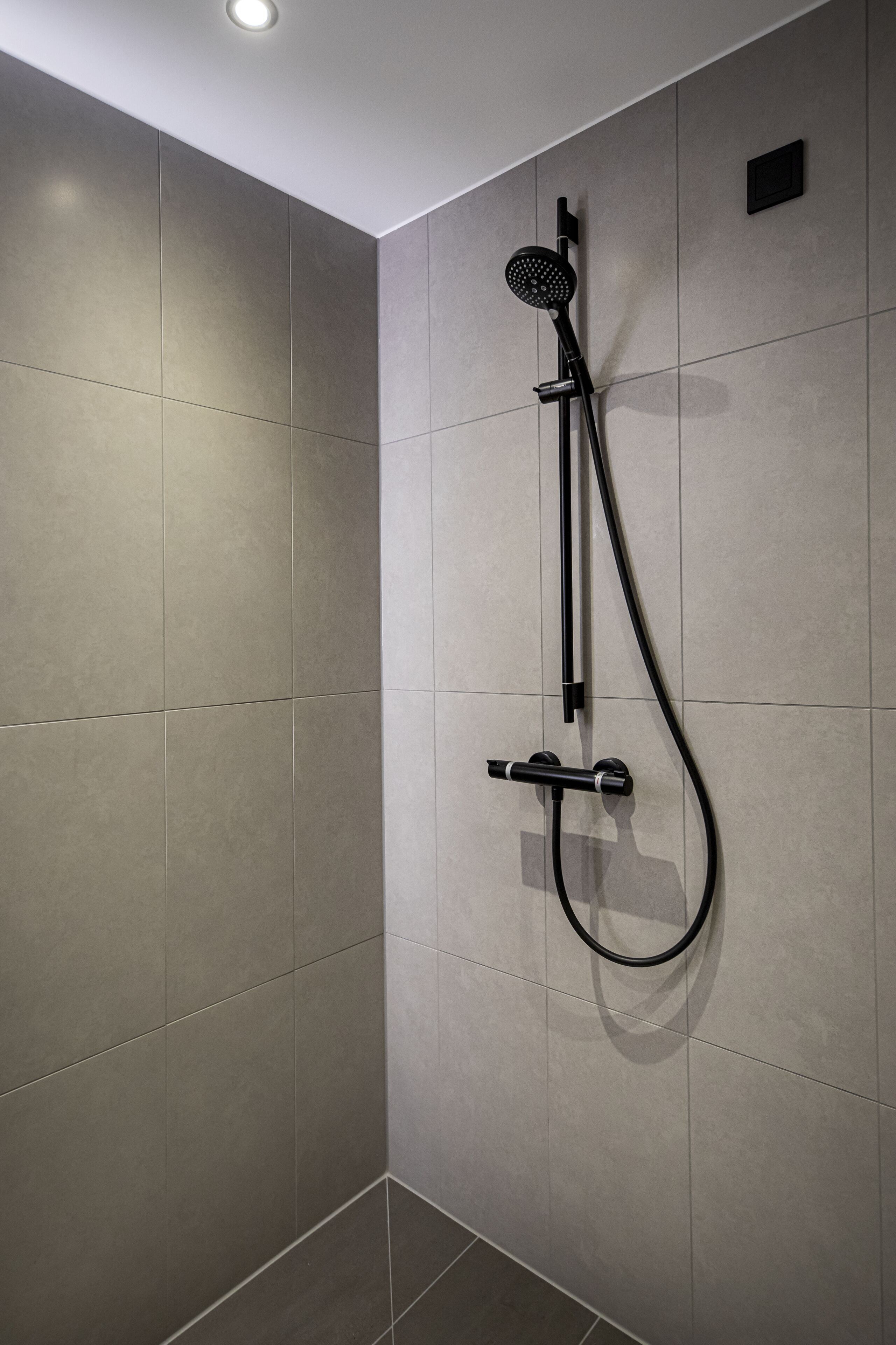 A modern shower with a handheld showerhead and a wall-mounted control panel.