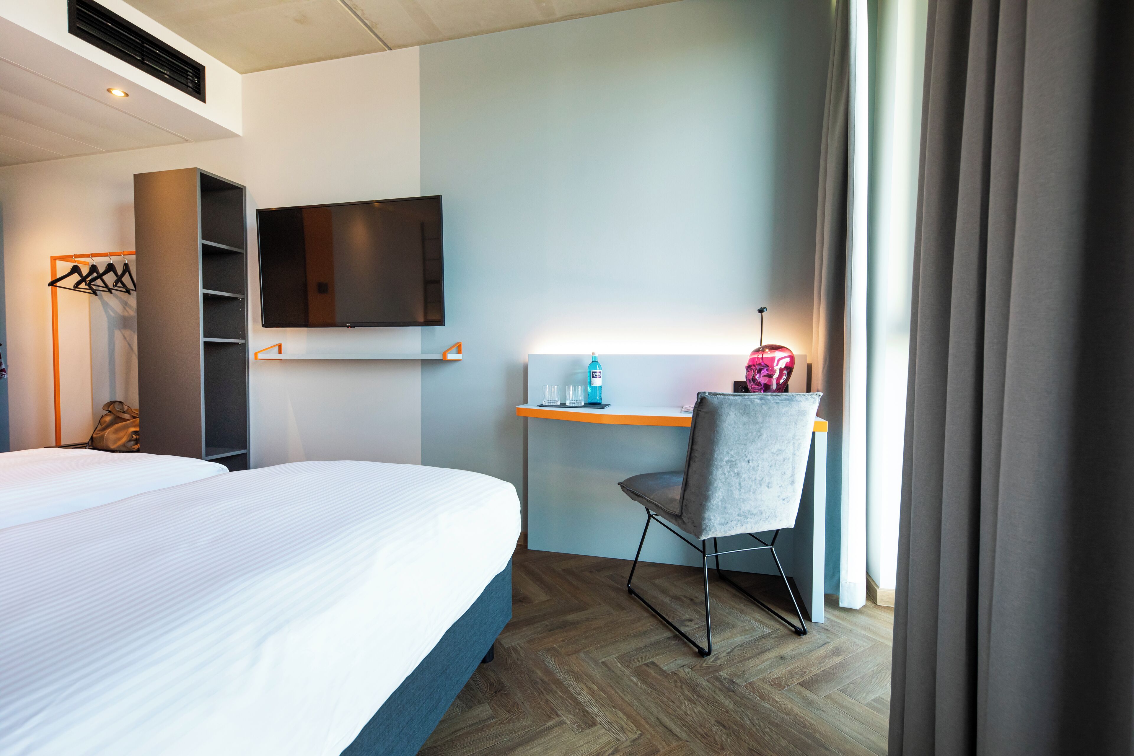 A hotel room with a bed, a desk, a chair, a TV, and a wardrobe.