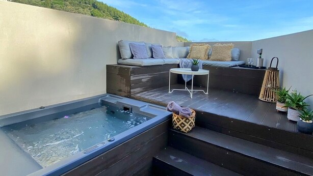 Une terrasse sur le toit équipée d’un jacuzzi, d’un espace salon et d’un escalier menant à un balcon.