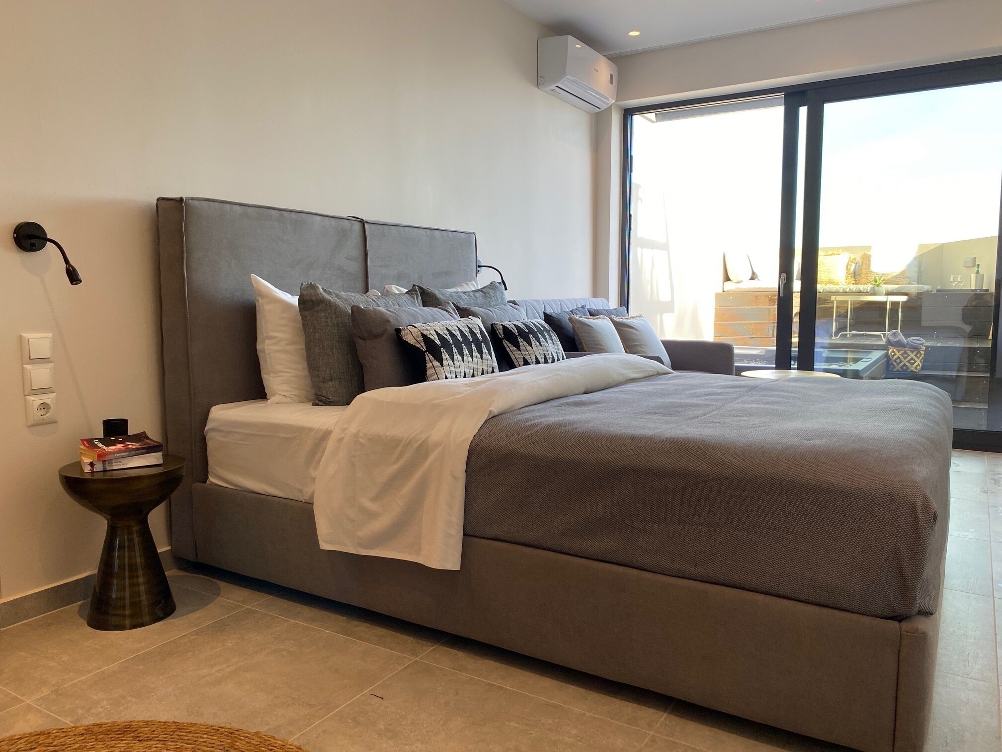 Un dormitorio moderno con una cama grande, ropa de cama gris y vistas a través de un ventanal.