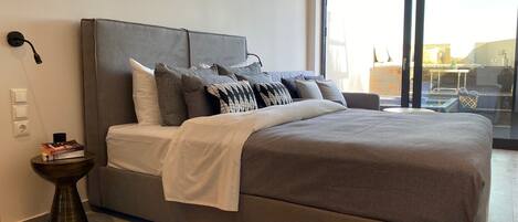 Un dormitorio moderno con una cama grande, ropa de cama gris y vistas a través de un ventanal.