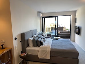Et moderne hotelværelse med en stor seng, et fjernsyn og udsigt til et udendørs område med et spabad og siddepladser.