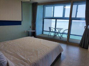 A hotel room with a large bed, a small round table with chairs, and a view of the sea through a large window. - Siesta (Namhae)