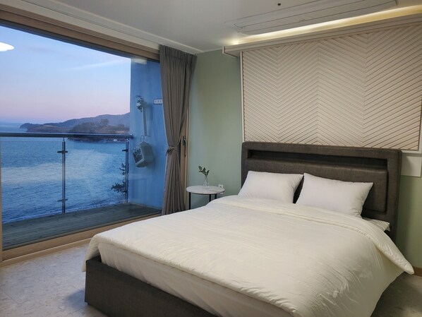 A bedroom with a large bed, a view of the sea, and a herringbone-patterned wall. - Siesta (Namhae)