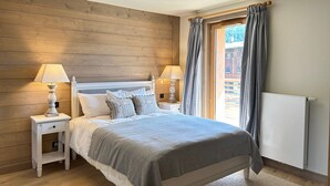 Una camera da letto con testiera in legno, due comodini con lampade, un letto con coperta grigia e una finestra con tende.