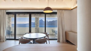 Un coin repas avec une table ronde et des chaises, de grandes fenêtres offrant une vue sur les montagnes et un plan d’eau, et une suspension au-dessus de la table.