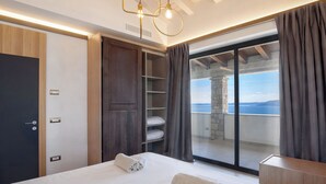 Une chambre moderne dotée d’un grand lit, d’une armoire, d’une bibliothèque intégrée et d’un balcon offrant une vue sur la mer.