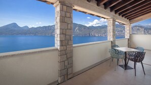 Un balcon doté de piliers en pierre, d’une table et de chaises, offrant une vue sur une étendue d’eau et des montagnes.