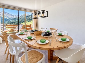 A round wooden dining table with chairs, plates, bowls, and a central light fixture.