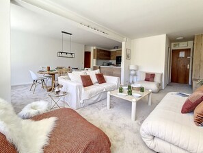A modern living room with a sofa, a coffee table, and a dining area with chairs and a table.