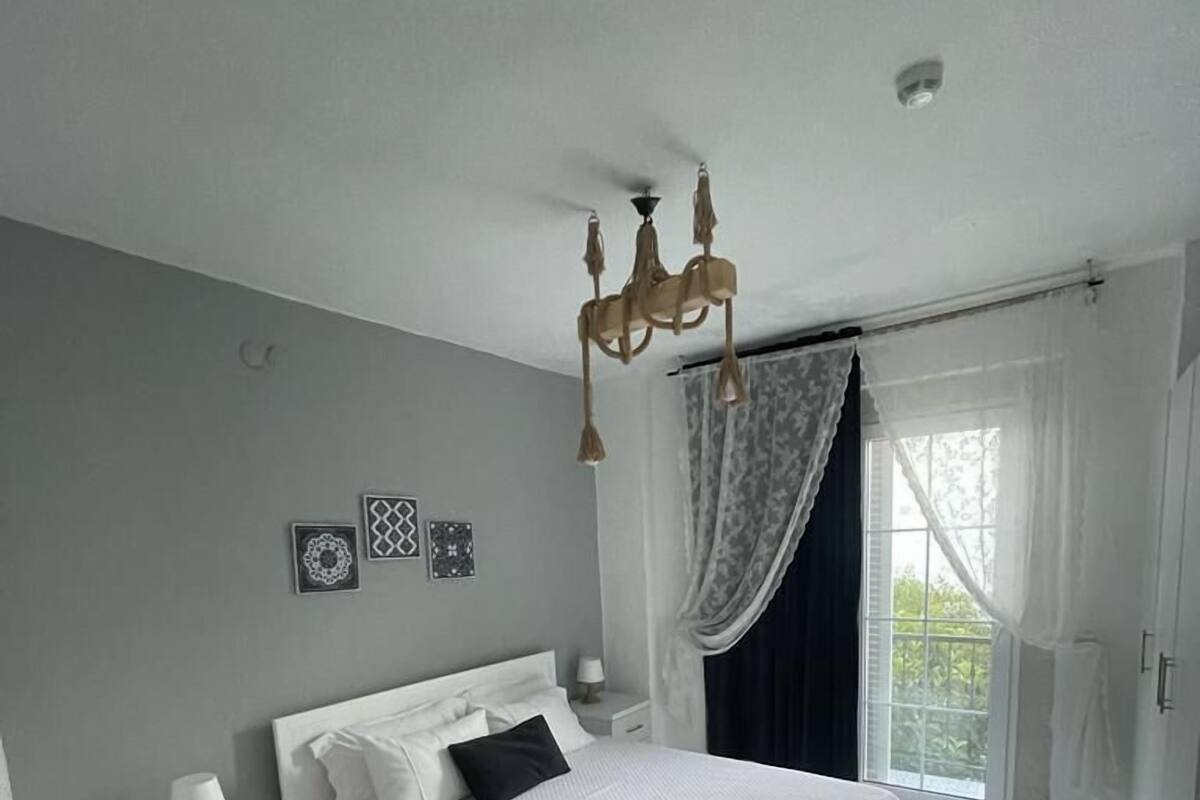 A bedroom with a large bed, a nightstand, a chair, and a window with curtains.