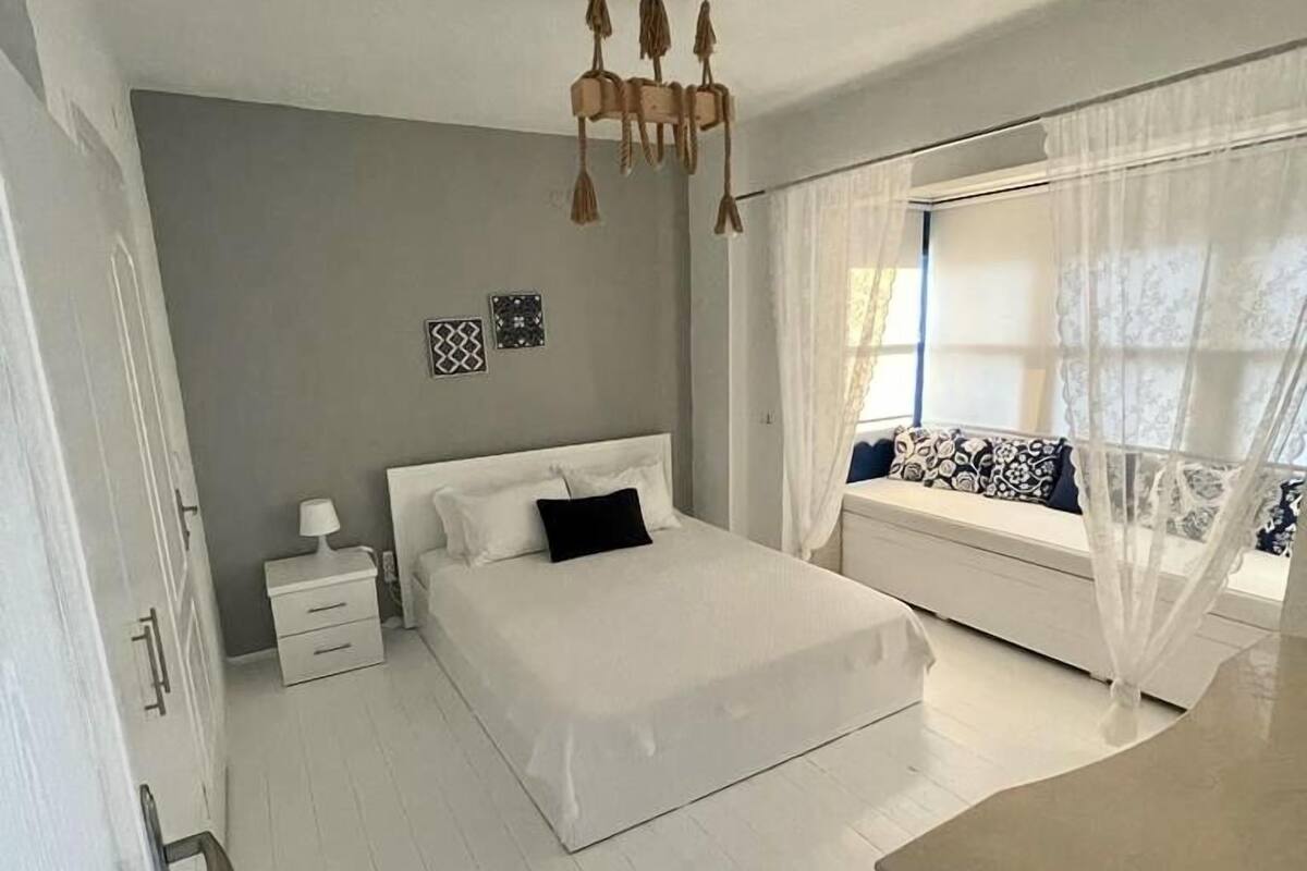 A bedroom with a bed, bedside table, and a window with curtains.