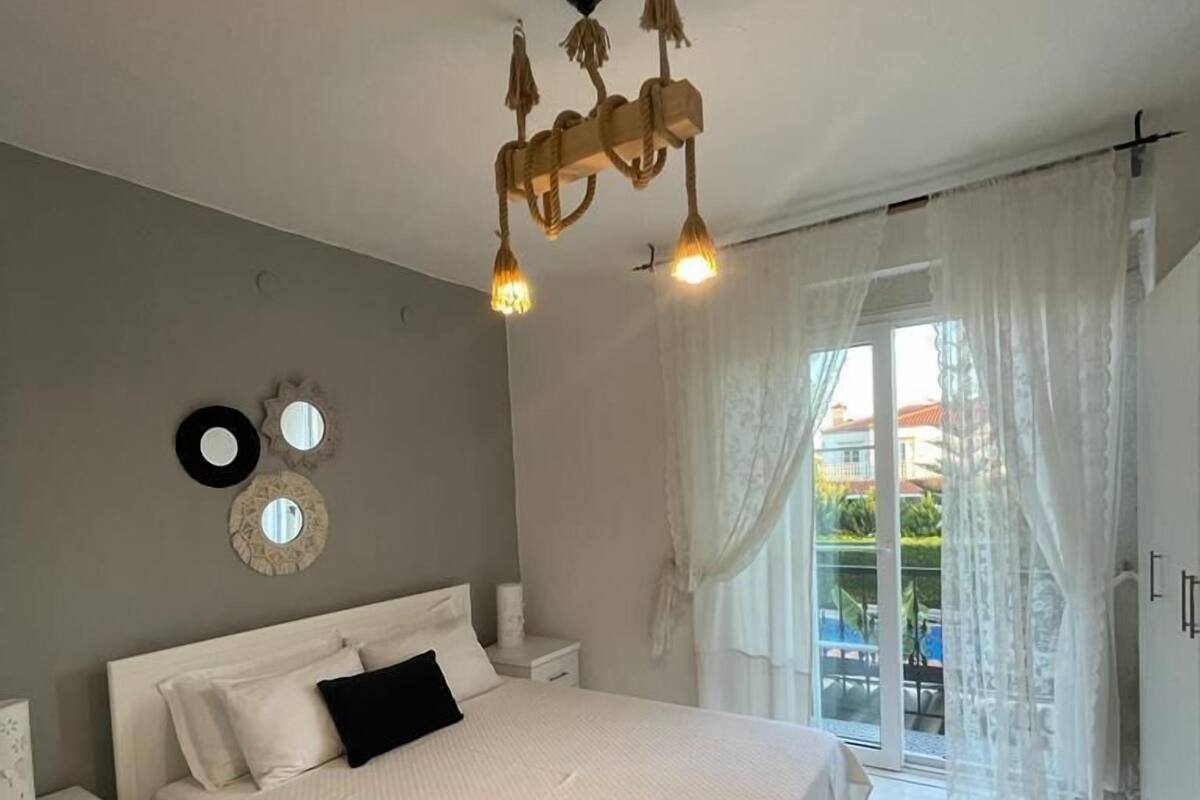 A bedroom with a large bed, a nightstand, a wall-mounted mirror, and a ceiling light fixture.