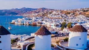 A coastal town with white buildings, a harbor with boats, and three prominent white towers with conical roofs. - Villa Cataleya (Μύκονος)