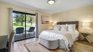 A bedroom with a large bed, a sliding glass door to a patio, a small table, and a chair.