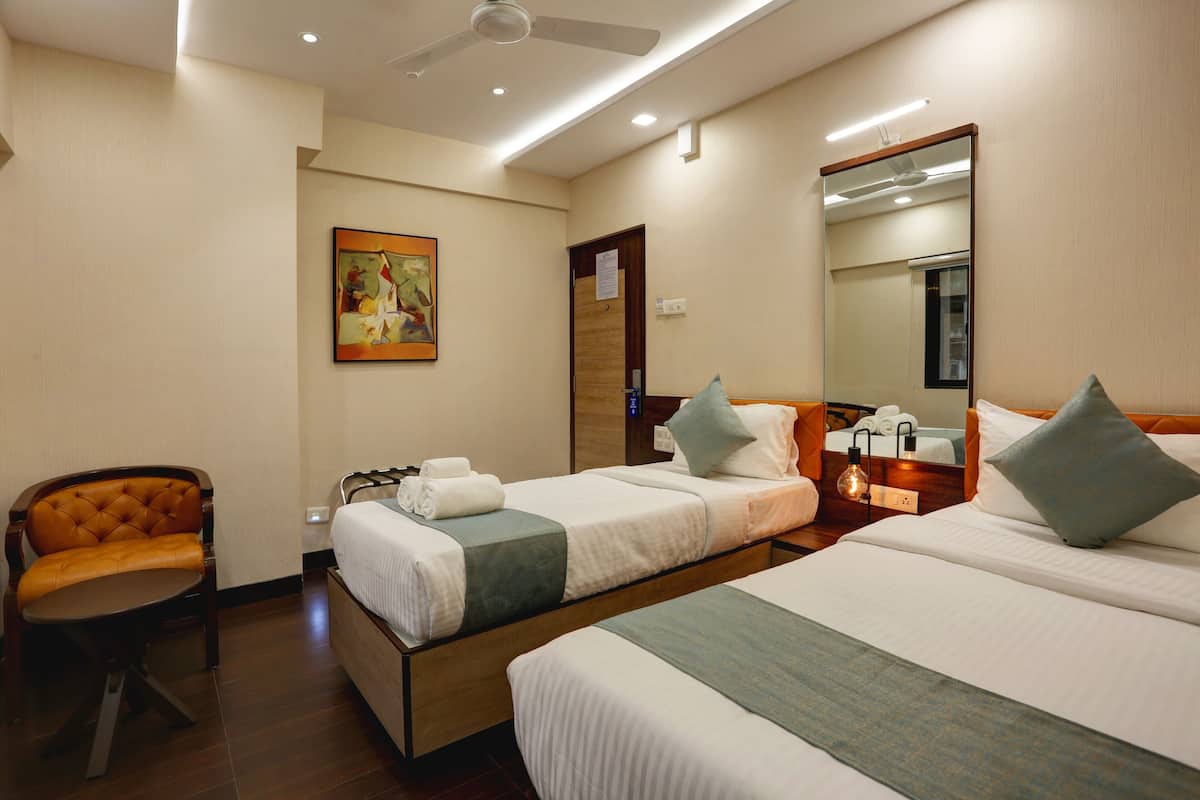 A hotel room with two beds, a chair, a painting, a mirror, and a ceiling fan.