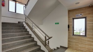 Una escalera con escalones de granito y barandillas metálicas, un extintor de incendios en la pared y un cartel de advertencia de videovigilancia.
