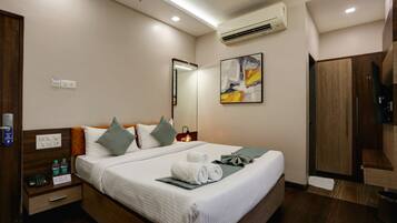 A hotel room with a neatly made bed, a bedside table with a phone and water bottles, a mirror, and a painting on the wall.