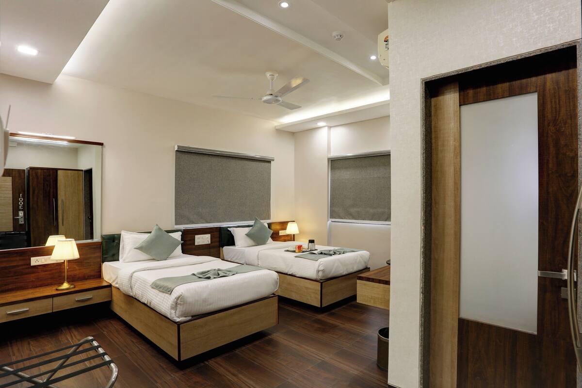 A hotel room with two beds, a desk, a chair, a mirror, and a ceiling fan.
