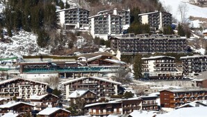 A ski resort with multiple buildings, including hotels and lodges, surrounded by snow-covered mountains and trees. - T2 + Sleeping Area 6 Pers, South, Wifi, La Clusaz (La Clusaz)