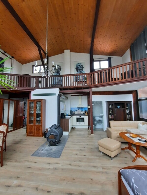 A spacious living area with a high ceiling, wooden beams, a balcony, a kitchen in the background, and a large cabinet. - Außergewöhnlich Wohnen in Weimar (Weimar)