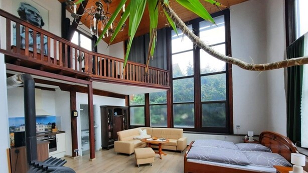 A spacious room with a large bed, a sofa, and a dining area. There is a balcony with a wooden railing and a view of the outdoors. - Außergewöhnlich Wohnen in Weimar (Weimar)