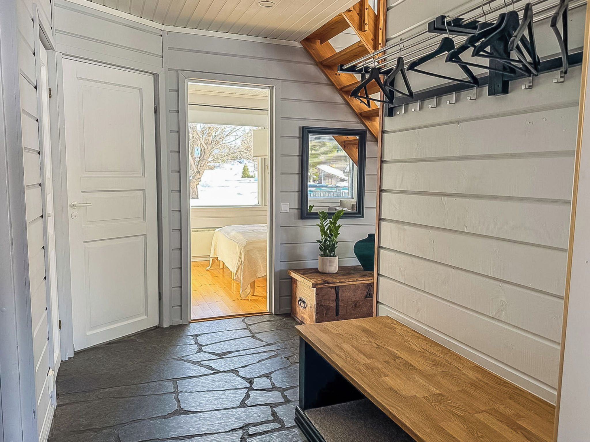 A hallway with a wooden bench, a coat rack, and a door leading to a room with a view.