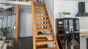 Un interior moderno con una escalera de madera que conduce a un dormitorio en buhardilla, una zona de cocina y una chimenea de piedra.