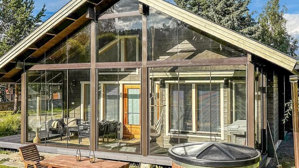 Una casa moderna de vidrio con terraza de madera y mobiliario exterior.