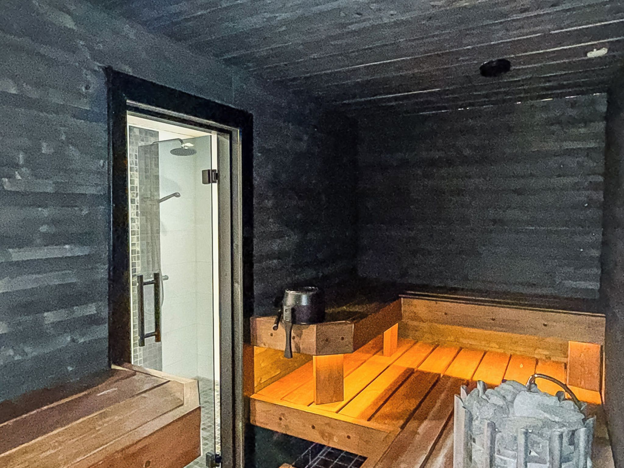 Un sauna con un banco de madera, una mesita y una puerta que da a otra zona.