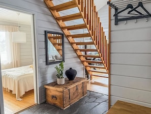 A staircase with wooden railings leading to an upper floor, a bedside table with a plant and vase, and a bed with a white cover.