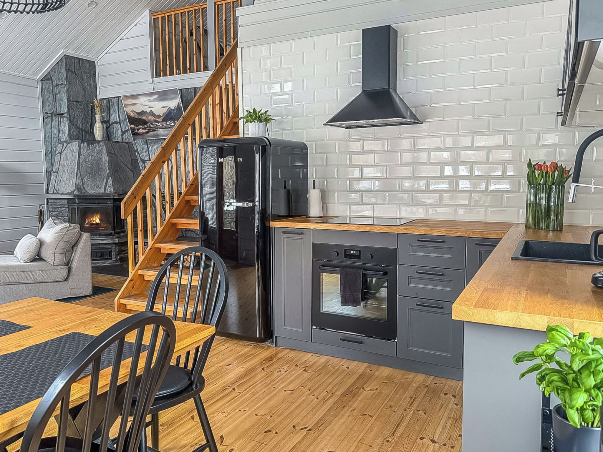A modern kitchen with a stone fireplace, wooden staircase, and a dining area with a table and chairs.