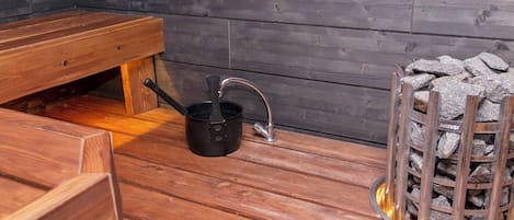 Een houten sauna met een bank, een zwarte kuip en een vuurkorf van steen.