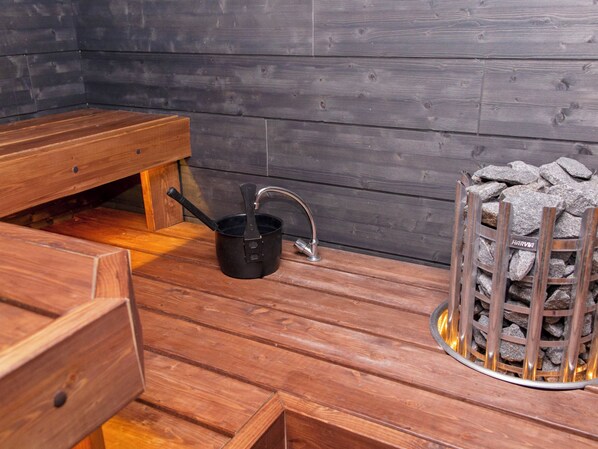 A wooden sauna with a bench, a black pot, and a stone fire pit.