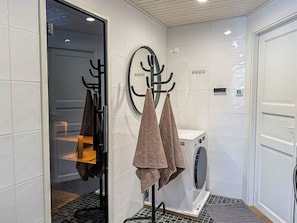 A compact bathroom with a washing machine, a towel rack, and a door.