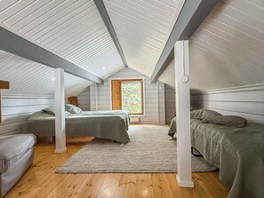 A room with two beds, a window, and wooden flooring.