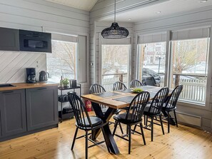 A modern kitchen with a dining area, large windows, and a view of the outside.
