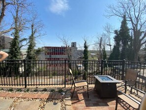 An outdoor patio area with a metal fence, two chairs, a table, and a view of a building in the background.