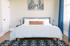 A bedroom with a bed, a cityscape painting, a nightstand, and a patterned rug. - 2 King Beds - Pool Table, Heart of Downtown LYH (Lynchburg)