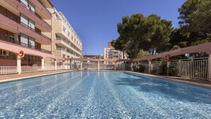 Una piscina con agua cristalina, rodeada por un edificio con balcones y una valla.