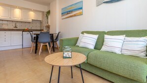 Una sala de estar moderna con un sofá verde, una mesa de centro redonda de madera y un cuadro con una escena de playa.