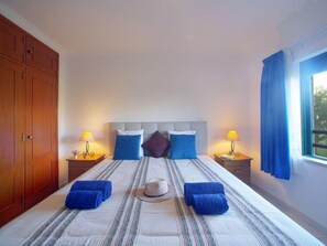Une chambre d’hôtel avec un grand lit, deux tables de chevet avec des lampes, une armoire et une fenêtre avec des rideaux.
