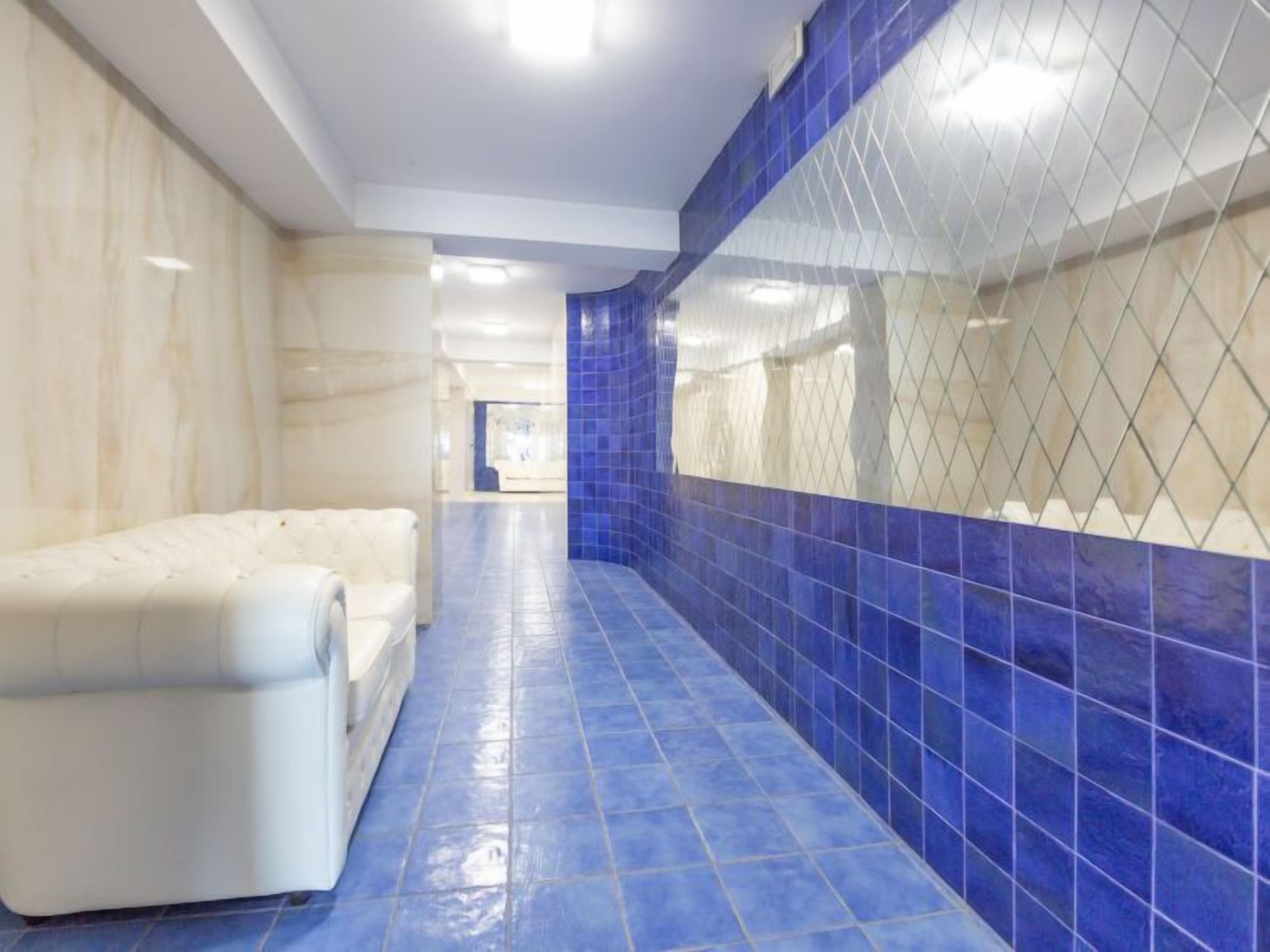 A corridor with a blue tiled floor and walls, leading to a room with a white cushioned seating area.